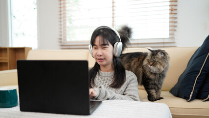 Young woman wearing headphones works on a laptop with a cat nearby