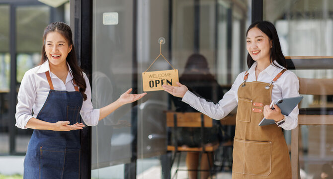 Portrait of two asian tan women barista wearing apron standing in open sign cafe. business owner employee Barista entrepreneur. SME entrepreneur seller business concept
 - Powered by Adobe