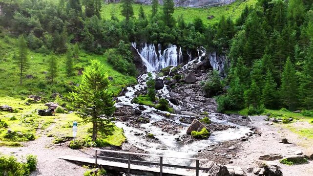 Waterfall at Lenk, Sibenf&auml;lle in Switzerland with cascading streams flowing through rocks, surrounded by green forest, alpine trees, and bright moss-covered terrain in a mountain valley environment