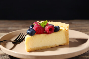 Piece of delicious cheesecake with fresh berries and fork on wooden table, closeup