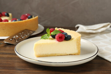 Piece of delicious cheesecake with fresh berries and mint served on wooden table, closeup