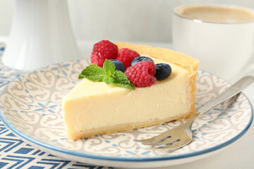 Piece of delicious cheesecake with fresh berries and mint served on white table, closeup
