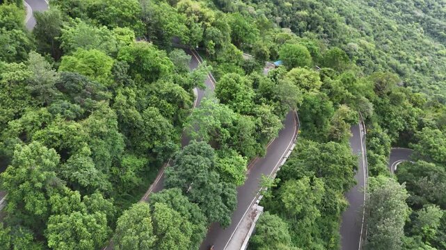 Scenic aerial footage of a winding road beginning its climb towards Kolli Hills, Tamil Nadu. Surrounded by rural fields and hilly dense forest slopes.