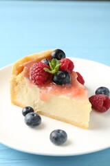 Piece of tasty cheesecake with berries and sauce on light blue wooden table, closeup