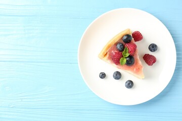 Piece of tasty cheesecake with berries and sauce on light blue wooden table, top view. Space for text