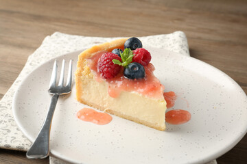 Piece of tasty cheesecake with berries and sauce on wooden table, closeup