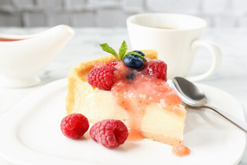 Piece of tasty cheesecake with berries and sauce served on white table, closeup