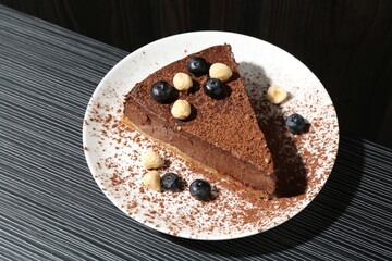 Piece of delicious chocolate cheesecake with nuts and blueberries on black textured table, above view