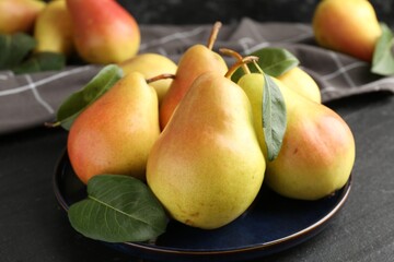 Many fresh pears and leaves on black table, closeup