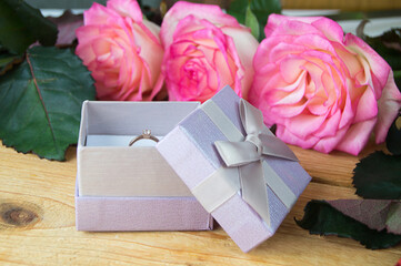 pink roses and engagement ring in a case on a wooden background