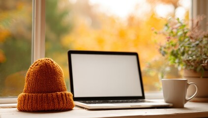 Autumn workspace by window with laptop, hat, and coffee