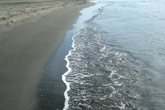 Gentle waves washing sea shore with sandy sand volcanic beach., creating tranquil ambiance with gentle rippling against coastal landscape during peaceful summer day. Wonderful wild nature landscape.