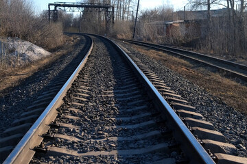 Obraz premium Railway, rails on street for public transport trains on nature. rail roads between trees, town buildings early spring. Urban transportation infrastructure with railroad tracks near city.