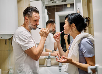 Portrait of a young japanese and white couple cleaning brushing their teeth in front of mirror in bathroom. Dental hygiene, youth, ove and beauty concepts