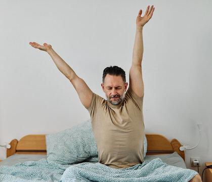 Middle-aged man relaxing and sleeping and waking up and stretching  in bed on a cozy morning in bedroom