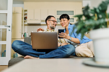 Portrait of a lovely young couple using a laptop and a mobile phone together and having fun sitting on sofa at home