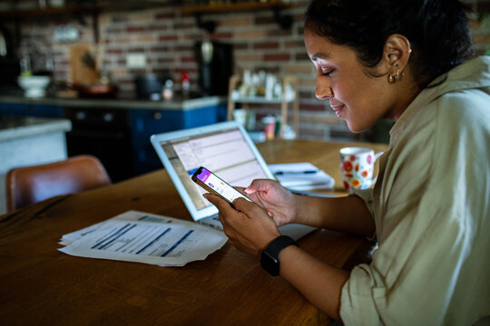 Woman using a mobile banking app on her smartphone while working on her finances