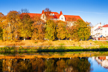Naklejka premium uzhhorod, ukraine - 31 oct, 2010: embankment of the river Uzh in autumn. beautiful view of old city with colorful foliage on trees in evening light. scenic european downtown in fall season