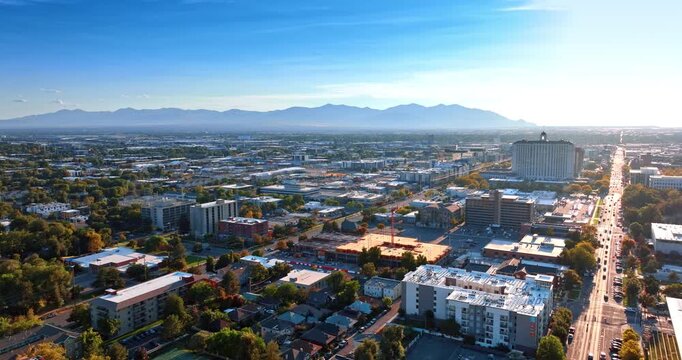 Bright sunlight dazzles the scenery of modern city. Mountain range silhouette in haze at backdrop. Salt Lake City, Utah, USA. Aerial perspective.