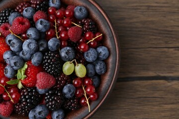 Different ripe berries in bowl on wooden table, top view. Space for text