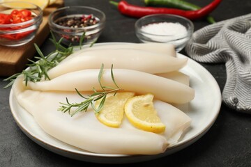 Uncooked squids with lemon slices, rosemary and spices on black table, closeup
