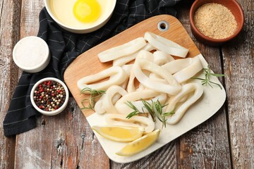 Uncooked squid rings, spices, yolk and bread crumbs on wooden table, flat lay