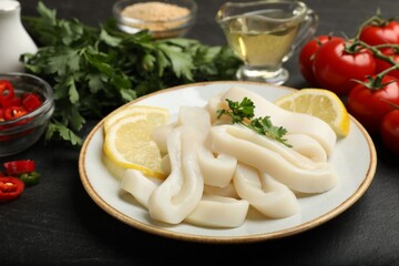 Raw squid rings, parsley, lemon and other products on dark textured table, closeup