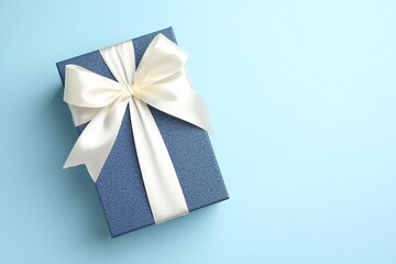 Gift box with beautiful bow on light blue background, top view. Space for text
