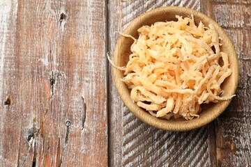 Dried squid shavings in bowl on color wooden table, top view. Space for text