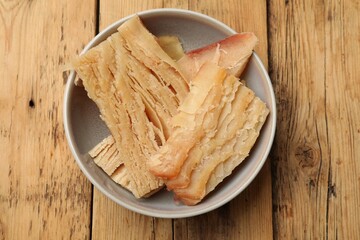 Pieces of tasty dried squid in bowl on wooden table, top view