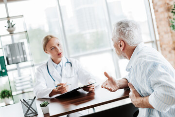 Obraz premium Elderly man receiving professional advice during a medical consultation in a brightly lit office with a caring doctor present