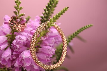 Stylish gold ring, bracelet and beautiful flowers against pink background, closeup. Space for text