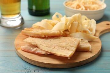 Dried squid snacks and beer on light blue wooden table, closeup