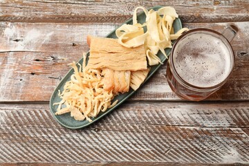 Dried squid snacks and glass mug of beer on color wooden table, flat lay
