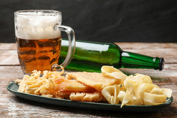 Dried squid snacks, bottle and glass mug of beer on color wooden table against dark textured background, closeup