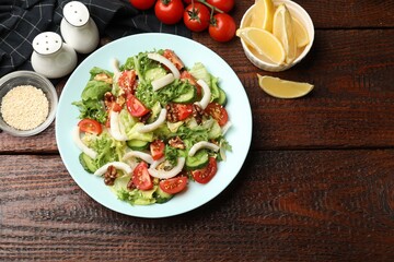Delicious salad with squid, vegetables and walnuts served on wooden table, flat lay. Space for text