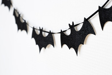 Black paper bats garland on white background. Halloween decoration, autumn party decor, spooky seasonal contrast backdrop for advertising and marketing design.