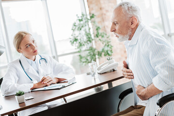 Doctor consulting elderly patient in modern clinic setting with concern and care for health...