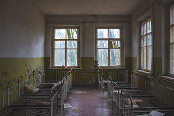 Desolate room in Chernobyl Nuclear Zone, with abandoned cots amidst chaos. Peeling paint and debris...