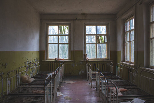 Desolate room in Chernobyl Nuclear Zone, with abandoned cots amidst chaos. Peeling paint and debris evoke a somber atmosphere. Possible old hospital setting, in decay.