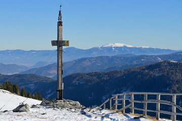 Summit cross in a ski resort in Austria with stunning distant view to snowy mountain ranges. Blue sky background with copy space. Ideal motif for advertising winter holidays and sports in Styria.