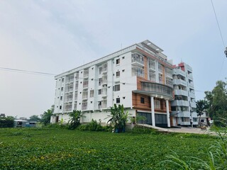 A pond filled with water lilies in front of a modern apartment building under a blue sky.
