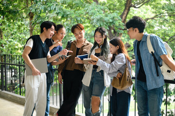 A diverse group of cheerful university students standing outdoors, discussing ideas and reviewing notes together with smiles and teamwork