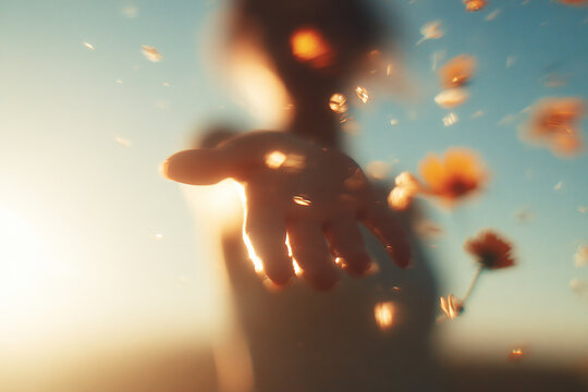 Woman opening hand releasing flowers into sunset