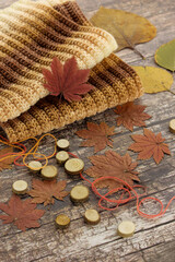 A warm knitted scarf for the cold seasons. Scarf and autumn maple leaves on a wooden background.