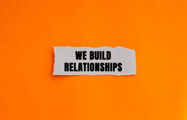 Naklejka premium We Build Relationships message written on ripped torn white paper piece on orange background. Conceptual We Build Relationships symbol. Copy space.