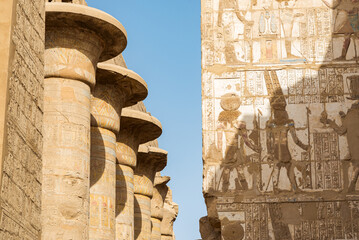 Columns row at the famous temple of Karnak, Luxor, Egypt, dedicated to the god Amon Ra. Wall full of hieroglyphics on the right. Blue sky on the background.