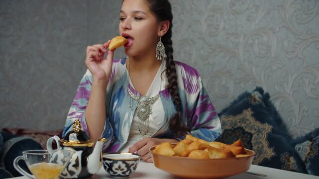 Young woman eating baursak with tea in traditional oriental interior