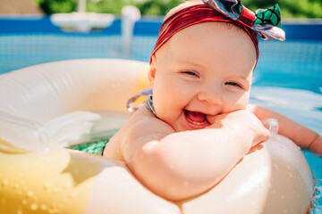 Adorable baby girl smiling while floating in pool ring, newborn child have fun