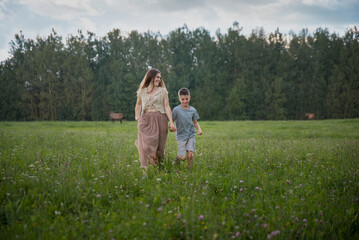 Mom and son are running in nature, holding hands. They look at each other and smile. The concept of family, child-rearing, and the relationship between mom and son